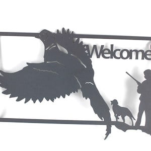 May include: Black metal wall art featuring a flying bird, a hunter with a rifle, and a dog. The word "Welcome" is cut out of the metal. The artwork is in the shape of a state.