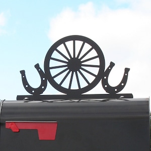 May include: Black metal mailbox topper with a wagon wheel and two horseshoes. The topper is mounted on a black mailbox.
