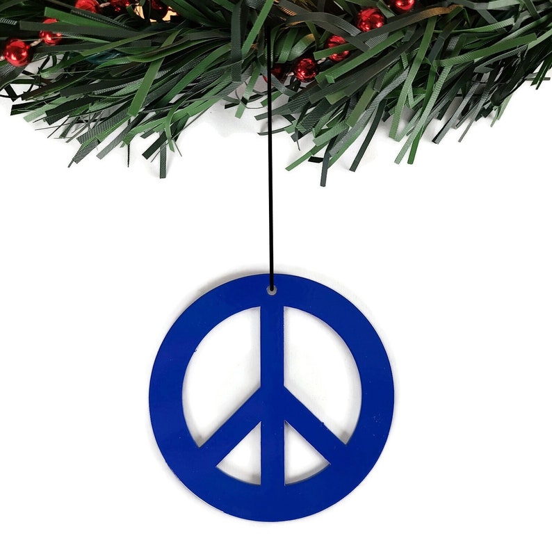 May include: A blue peace sign ornament hanging from a green garland with red berries.