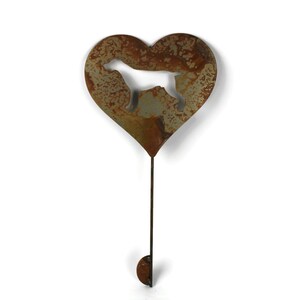 May include: A rustic metal garden stake featuring a heart shape with a dog silhouette cutout. The heart is attached to a long, thin rod with a small, rounded hook at the bottom. The metal has a weathered, brown and green patina.