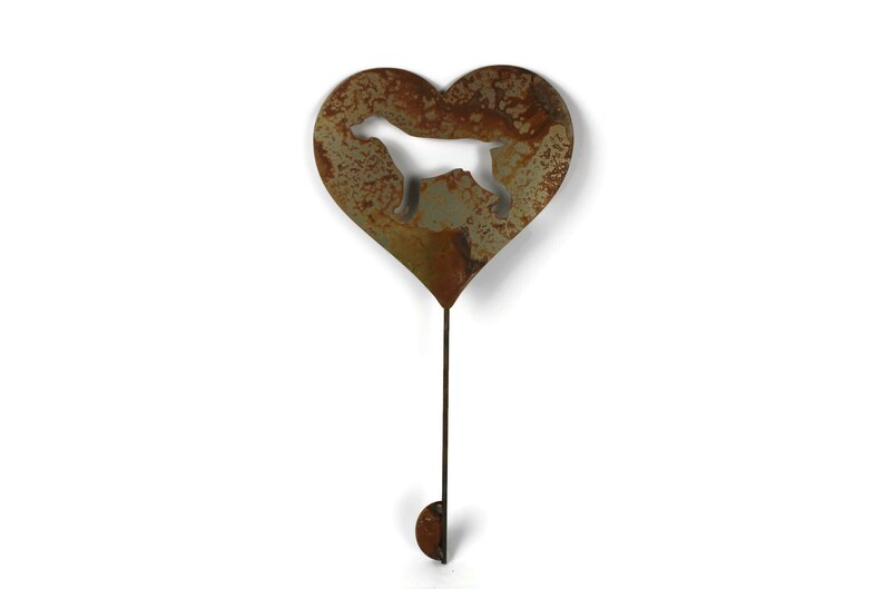 May include: A rustic metal garden stake featuring a heart shape with a dog silhouette cutout. The heart is attached to a long, thin rod with a small, rounded hook at the bottom. The metal has a weathered, brown and green patina.