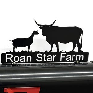 May include: Black metal sign with the words "Roan Star Farm" in white, featuring silhouettes of a goat and a longhorn steer. The sign is mounted on a black mailbox.