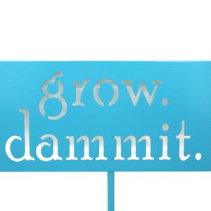 May include: A light blue sign with the words "grow. dammit." in white lettering.