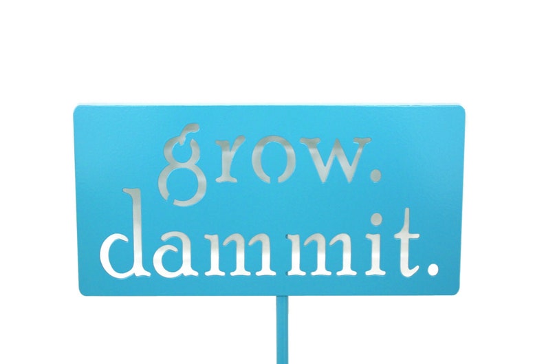 May include: A light blue sign with the words "grow. dammit." in white lettering.