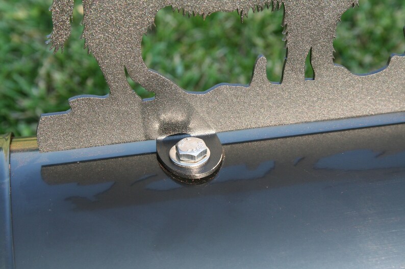 Puede incluir: Primer plano de un buz&oacute;n de metal con una tapa decorativa de metal que presenta la silueta de tres animales. El buz&oacute;n es negro y la tapa es plateada. Se ve un tornillo plateado en el buz&oacute;n.