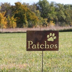 Patches with a paw in the upper right corner, is placed in a yard. You can see the grass through the name and paw.