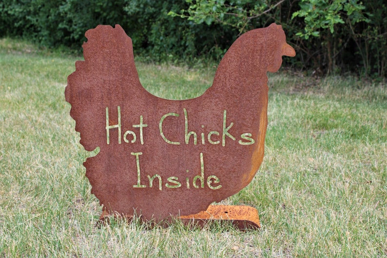 May include: A rusty metal chicken silhouette with the words "Hot Chicks Inside" written on it. The chicken is standing on a grassy lawn.