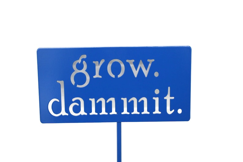 May include: A blue metal sign with the words "grow. dammit." in white lettering.