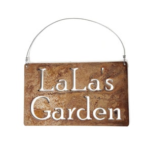 May include: A rusty metal sign with a wire hanger. The sign says "LaLa's Garden" in white lettering.