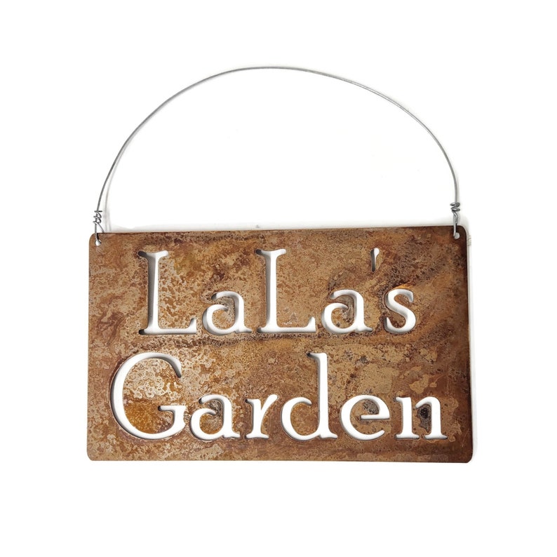 May include: A rusty metal sign with a wire hanger. The sign says "LaLa's Garden" in white lettering.