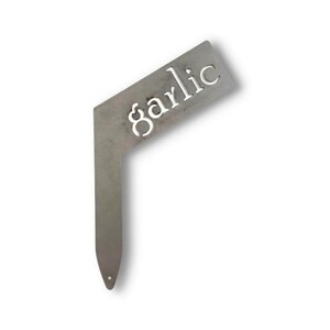 May include: A metal garden marker with the word "garlic" cut out. The marker is shaped like a right angle with a pointed end.