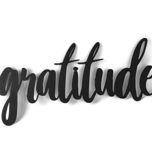 May include: Black metal wall decor with the word "gratitude" written in a cursive font.