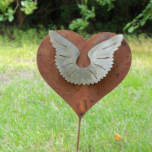 May include: A rusty metal heart-shaped garden stake with a pair of silver wings attached to the center.