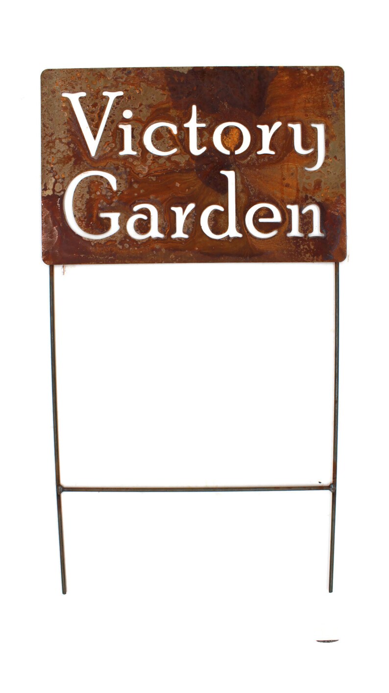 May include: A rectangular, weathered metal garden stake with the words "Victory Garden" cut out in white lettering. The stake has a rusty brown finish and is supported by two thin metal rods.