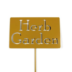 May include: A golden-yellow metal garden stake with the words "Herb Garden" cut out. The sign is rectangular and mounted on a thin, gold-colored rod. Ideal for marking herbs in a garden.