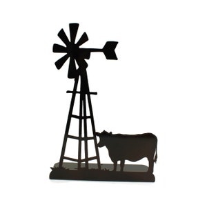 May include: A black metal silhouette sculpture featuring a tall windmill with a multi-blade fan and a tail vane, positioned next to a cow standing on a flat base. The design is a flat, two-dimensional cutout made of dark metal.