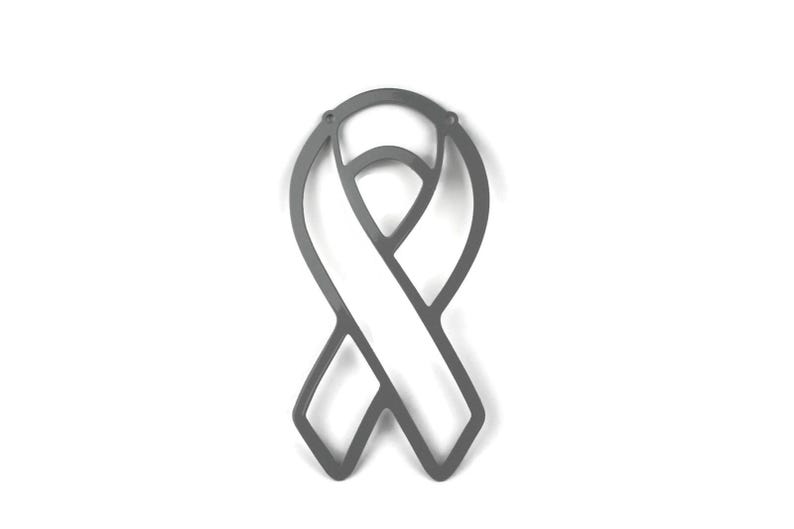 May include: A gray metal ribbon cutout, a symbol of awareness. The ribbon is a stylized design with a loop and a vertical bar, set against a white background. The cutout has a smooth, matte finish and is likely used for decorative purposes.