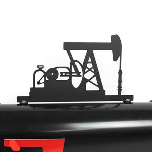 May include: Black metal oil derrick silhouette mounted on a black mailbox. The mailbox has a red flag and a curved top. The oil derrick is a decorative accent.