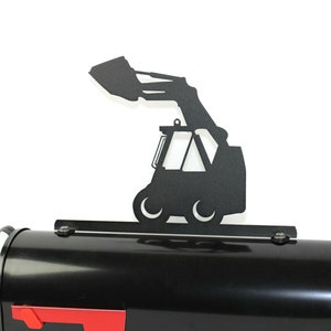 May include: Black metal mailbox topper featuring a silhouette of a skid steer loader with the bucket raised. The topper is mounted on a black mailbox.