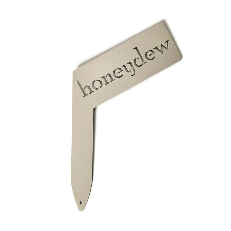 May include: A metal garden marker with the word "honeydew" cut out. The marker is a light beige color and has a pointed end.