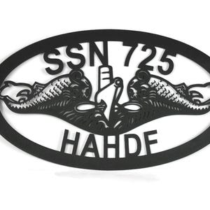 Puede incluir: Un letrero de pared ovalado de metal negro con un dise&ntilde;o recortado de la insignia de guerra submarina, que incluye dos delfines flanqueando la proa de un submarino. El texto SSN 725 est&aacute; arriba y el texto HAHDF abajo en el &oacute;valo.