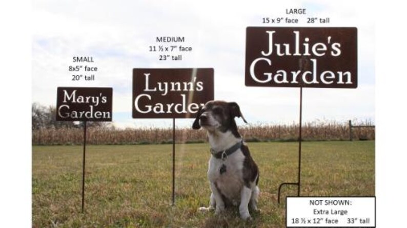 May include: Three metal garden signs with the names "Mary's Garden", "Lynn's Garden", and "Julie's Garden" are displayed in a grassy field. The signs vary in size, with the largest measuring 15 x 9 inches. A dog sits in front of the signs.