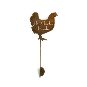 May include: A rusty metal chicken silhouette with the words "Hot Chicks Inside" written in white chalk on the body. The chicken is attached to a long, thin metal rod with a round base.