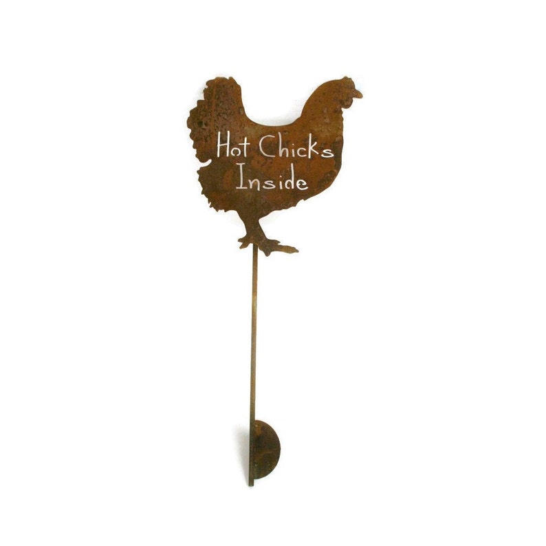 May include: A rusty metal chicken silhouette with the words "Hot Chicks Inside" written in white chalk on the body. The chicken is attached to a long, thin metal rod with a round base.