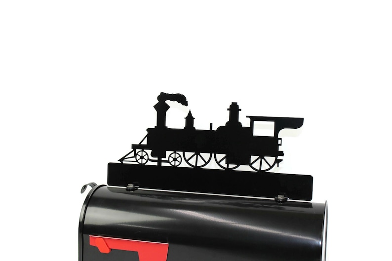 May include: Black metal train silhouette mailbox topper. The topper features a detailed outline of a classic steam engine with smoke billowing from the smokestack. The topper is mounted on a black mailbox with a red flag.