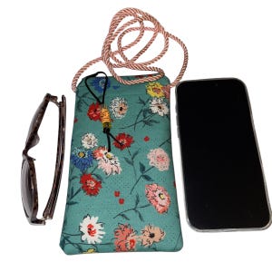 May include: A teal floral print crossbody phone bag with a matching rope strap. The bag features a black drawstring with decorative beads. A pair of sunglasses and a smartphone are next to the bag.