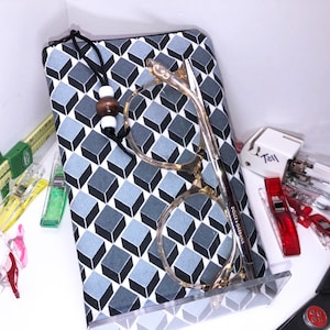 May include: A black and white geometric patterned zippered pouch with a black cord and wooden bead. A pair of clear framed glasses with the text "Dolce & Gabbana" on the arm is inside the pouch.