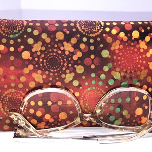 May include: A patterned glasses case with a matching pair of eyeglasses. The case is a dark red with a repeating pattern of yellow, orange, and green circles. The eyeglasses have a light-colored frame.