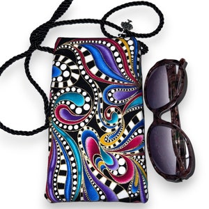 May include: A black fabric crossbody bag with a colorful paisley pattern. The bag has a black rope strap and a silver charm. A pair of brown sunglasses are next to the bag.