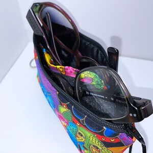 May include: A colorful zippered pouch with a black zipper and two pairs of glasses inside. The pouch has a bright, multi-colored pattern with flowers, hearts, and other designs.