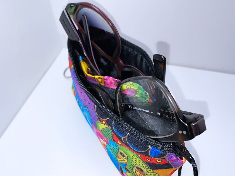 May include: A colorful zippered pouch with a black zipper and two pairs of glasses inside. The pouch has a bright, multi-colored pattern with flowers, hearts, and other designs.