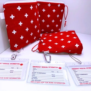 May include: Three red zippered pouches with white plus signs printed on them. The pouches are on a white surface with three clear plastic card holders that say "Emergency Medical Information" with spaces to fill in personal information.