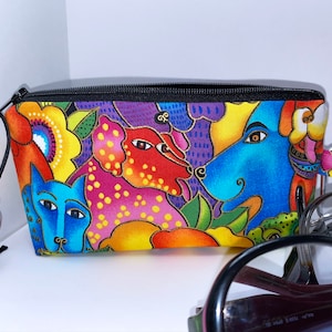 May include: A colorful zippered pouch with a black zipper and a black cord with a wooden bead. The pouch features a whimsical design of dogs and flowers in shades of blue, red, yellow, green, and purple.
