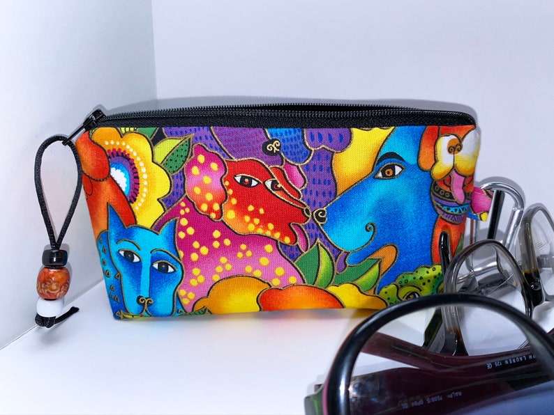 May include: A colorful zippered pouch with a black zipper and a black cord with a wooden bead. The pouch features a whimsical design of dogs and flowers in shades of blue, red, yellow, green, and purple.