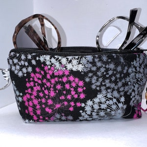 May include: Black zippered pouch with a floral print in shades of pink, gray, and white. The pouch has a silver key ring and a pink tassel with a wooden bead.