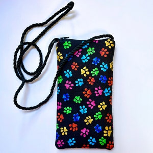 May include: Black crossbody bag with a colorful paw print pattern. The bag has a long adjustable strap.
