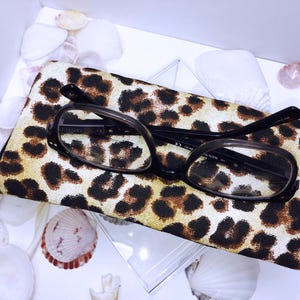 Pode incluir: Um estojo para &oacute;culos de estampa de leopardo com um par de &oacute;culos de arma&ccedil;&atilde;o preta dentro.