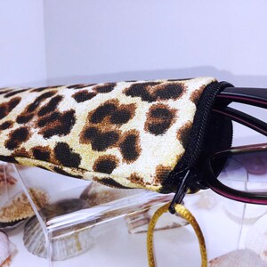 Pode incluir: Um estojo para &oacute;culos de estampa de leopardo com fecho de correr. O estojo cont&eacute;m &oacute;culos de sol pretos com lentes castanhas.