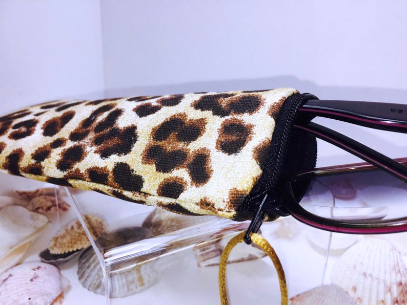Pode incluir: Um estojo para &oacute;culos de estampa de leopardo com fecho de correr. O estojo cont&eacute;m &oacute;culos de sol pretos com lentes castanhas.
