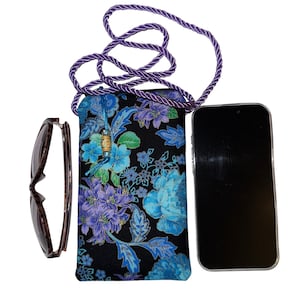 May include: A black floral print crossbody phone bag with a purple rope strap. The bag features blue and purple flowers. Sunglasses and a smartphone are next to the bag.