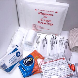 May include: A first aid kit with various supplies, including gauze dressings, bandages, a roll of gauze, pain relief tablets, and an emergency medical information card. The kit is labeled "Walgreens" and includes the text "Gauze Dressings".