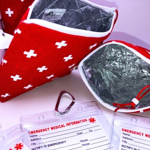 May include: Two red zippered pouches with white crosses and a silver lining. The pouches are open to show the silver lining. There are three clear plastic card holders with the text "EMERGENCY MEDICAL INFORMATION" and a red cross symbol. The card holders have spaces for name, address, city, state, zip, phone, and notify in emergency.