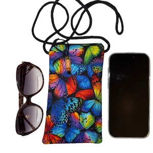 May include: A colorful phone crossbody bag with a vibrant butterfly pattern in shades of blue, purple, orange, and yellow. The bag has a black cord strap and a decorative wooden bead. Sunglasses are next to the bag.