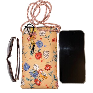 May include: A floral print phone crossbody bag with a brown rope strap, next to a pair of sunglasses and a smartphone. The bag features a beige background with red, blue, and white flowers.