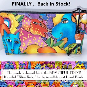 May include: A colorful zippered pouch with a whimsical design featuring dogs and flowers. The pouch is made of fabric and has a black zipper and a tassel. The text "FINALLY... Back in Stock!" is printed above the pouch. The text "This pouch is also available in this BEAUTIFUL PRINT! It's called "Feline Frolic," by the incredible artist Laurel Burch." is printed below the pouch.