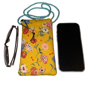 May include: A yellow floral print phone bag with a teal rope strap, sunglasses, and a smartphone. The bag features a drawstring closure and a decorative bead. The sunglasses have a dark frame.